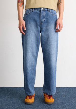 Light blue denim jeans with a straight leg fit, five pockets, and a button closure. Worn with orange and burgundy sneakers.