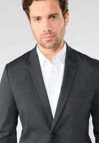 Blazer texturé gris foncé avec un bouton unique, revers crantés et poche poitrine, porté sur une chemise blanche à col.