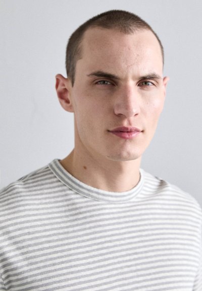 Camiseta de cuello redondo a rayas con rayas horizontales en gris claro y blanco, textura suave y diseño sencillo, llevada por un modelo.