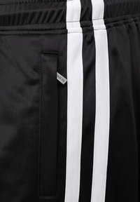 Crne atletske šortse s bijelim bočnim prugama, teksturiranim materijalom, elastičnom pojasom i malom oznakom s logom blizu džepa.