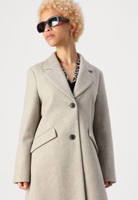 Cappotto in lana beige con un design strutturato, rever a punta, due tasche frontali e due bottoni. Tessuto texturizzato con una finitura liscia.
