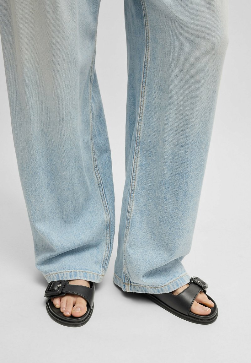 Svarta sandaler med spänne, bärs med ljusblå, löst sittande denimjeans med en urtvättad textur och avslappnad passform.