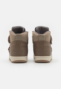 Chaussures montantes marron en suédine et cuir, avec des sangles Velcro, des accents texturés et une semelle en caoutchouc beige.