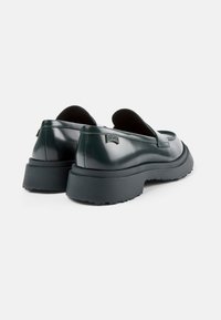 Dunkelgrüne Lacklederschlupfschuhe mit einer dicken schwarzen Sohle und einem strukturierten Profil. Verfügt über eine dezente Logoakzentuierung in der Nähe der Ferse.