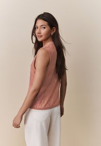 Top senza maniche corallo con motivo testurizzato, scollo arrotondato e lieve lucentezza, abbinato a pantaloni bianchi a gamba larga.