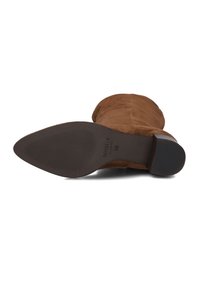 Bruine suède enkellaars met een ronde neus, lage blokhak en een gekartelde rubberen zool met horizontale groeven en merklogo op de binnenzool.