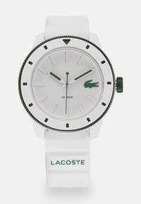 Λευκό ρολόι με πράσινες λεπτομέρειες, με υφή στη διάταξη του καντράν, μεγάλες ενδείξεις ωρών και ανθεκτικό λουρί από καουτσούκ με ανάγλυφο το "LACOSTE."