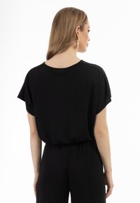 Schwarzer Jumpsuit mit kurzen Ärmeln, lockerer Passform, elastischem Bund und weichem Stoff. Schlichtes Design ohne sichtbare Muster oder Akzente.