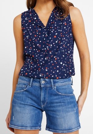 Mouwloze marineblauwe blouse met rood, wit en roze bloemenprint, gecombineerd met middenblauwe denim shorts met omslag.