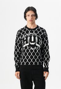 Sort strik-knit sweater med et hvidt diamantmønster, et stort "HUF" logo i centrum samt ribbede mansjetter og kant.