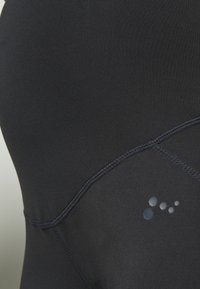 Černé sportovní oblečení vyrobené z hladkého, elastického materiálu s přiléhavým střihem. Výrazným prvkem je potištěné logo s barevnými body v přechodu.