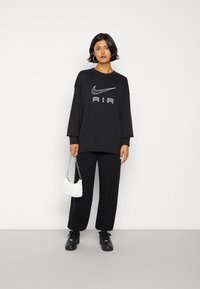 Black oversized sweatshirt with white Nike logo and "AIR" text, paired with black pants, black sneakers, and a small white quilted handbag.