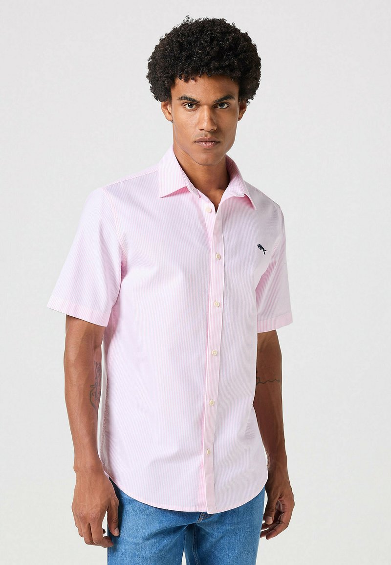 Camicia a maniche corte con bottoni di colore rosa chiaro, decorata con sottili righe bianche e un piccolo logo ricamato sul petto. Materiale in cotone, texture liscia.