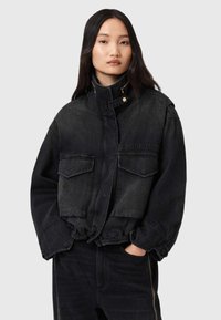Veste en denim noir coupée avec un col haut, deux poches avant et un ourlet élastique. Dotée d'une fermeture à boutons et d'une texture légèrement usée.