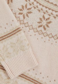 Krémový pletený sveter s svetlohnedými vzormi snehových vločiek a geometrickými vzormi, so zúženými manžetami a príjemnou textúrou.