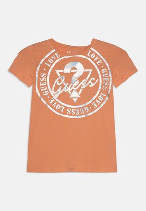 Orange kortærmet t-shirt med sølvmetallic "Guess" logo, et spørgsmålstegn og ordene "Guess Love" gentaget i et cirkulært design.