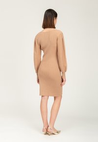Rippkleid im Bodycon-Stil in Hellbraun, mit langen Ärmeln und rundem Ausschnitt, das knapp über dem Knie endet. Goldfarbige Hardware-Details am Rücken.