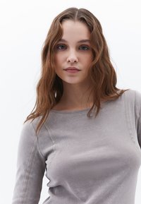 Maglietta a maniche lunghe grigio chiaro con scollo a girocollo, caratterizzata da una texture liscia e dettagli di cucitura sottili lungo le cuciture.