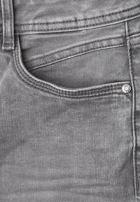 Gros plan d'une poche de jean en denim gris avec des coutures visibles et un petit rivet métallique sur le bord de l'ouverture de la poche.