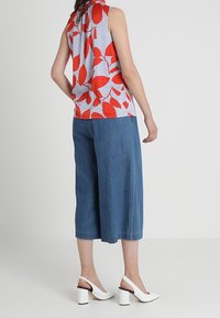 Bezramienna bluzka w czerwony kwiatowy wzór na białym i niebieskim tle w paski, zestawiona z szerokimi dżinsowymi kulotami i białymi butami na słupku.