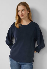 Felpa blu navy con girocollo, maniche lunghe e tessuto morbido. Presenta una vestibilità rilassata e una sottile spaccatura laterale all'orlo.