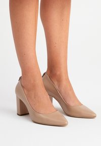 Beige korkokenkiä, joissa on teräväkärkinen muotoilu ja sileä pinta. Paksut korot ja minimalistinen muotoilu, jossa on hienovarainen takaleikkaus.