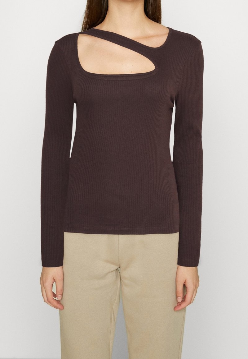 Brązowa, prążkowana bluzka z długim rękawem, charakteryzująca się unikalnym wycięciem na lewym ramieniu, podkreślająca fakturę i dopasowany krój.