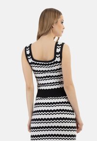 Top tricotat cu model într-o zigzag alb-negru, cu decolteu pătrat și talie ajustată. Textură netedă, design fără mâneci.
