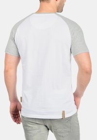 Short-sleeve raglan t-shirt in white with gray sleeves, made of soft cotton. Features a rear tag and simple, clean design.