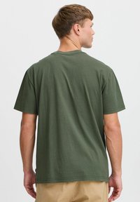 Camiseta de algodón verde oliva con mangas cortas, cuello redondo y corte relajado. Diseño minimalista sin patrones ni logotipos visibles.