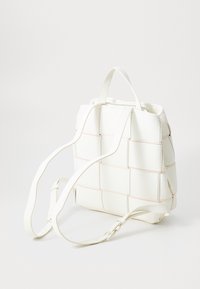 Zaino intrecciato bianco realizzato in materiale sintetico, con spalline regolabili e dettagli di cucitura leggeri. Forma compatta quadrata, senza parti metalliche visibili.
