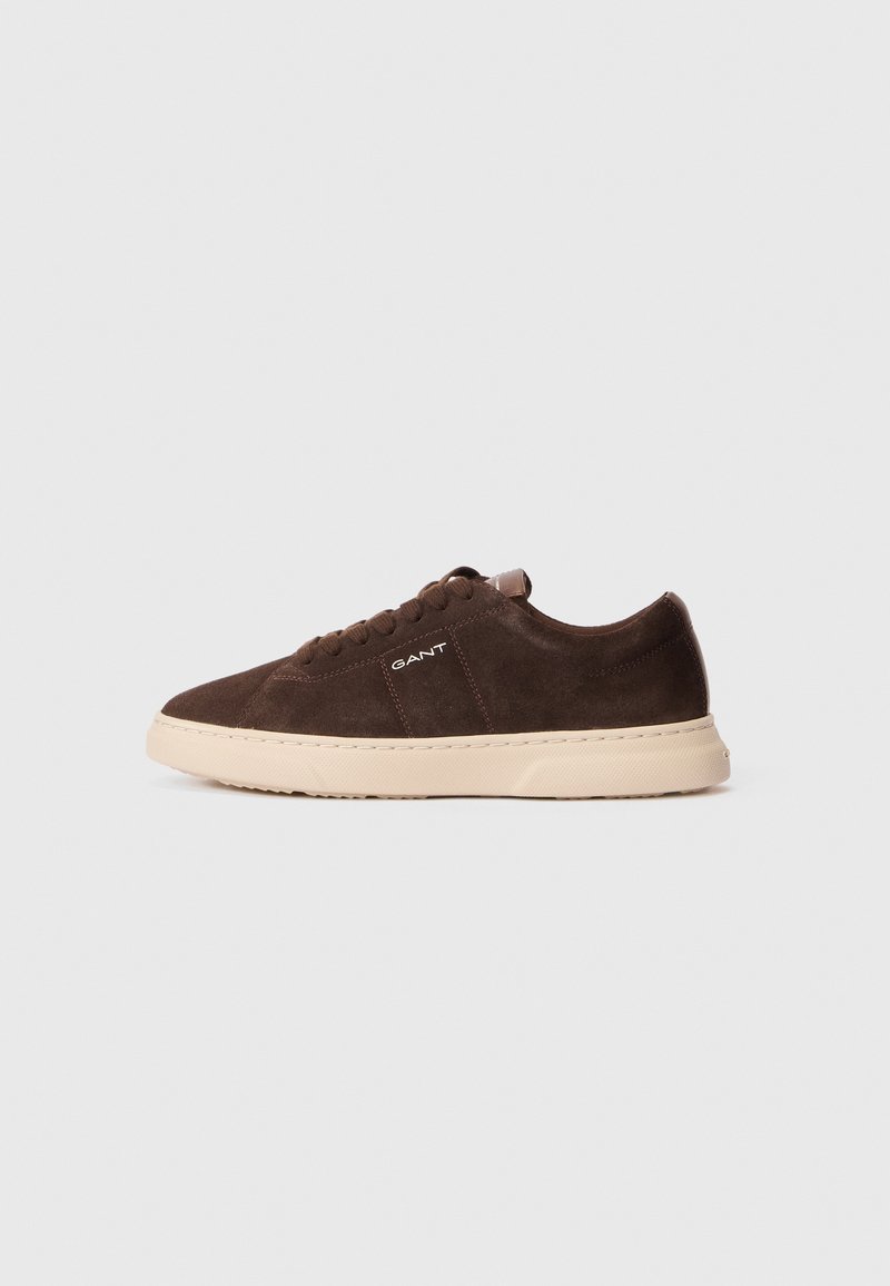 Brown suede sneaker with a cream rubber sole, featuring a rounded toe, lace-up design, and logo detail on the side.