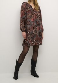 Šaty s červeno-černým vzorem, dlouhými rukávy, V-výstřihem a květinovými motivy. Nosené s černými kovbojskými botami a průsvitnými černými punčochami.