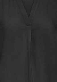 Vêtement noir à encolure en V avec des coutures visibles le long du col et une couture verticale au centre devant.