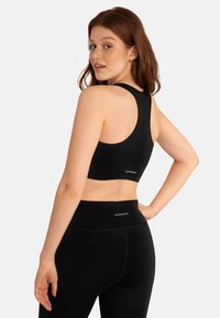 Zwarte sport-bh met een geribbelde structuur, racerback ontwerp en logodetail. Draag met bijpassende zwarte high-waisted leggings.