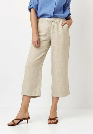 Beige linen cropped pants with an elastic waistband, drawstring detail, and side pockets, paired with brown strappy heels.