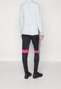 Světle modrý top s dlouhým rukávem a vysokým límečkem, kombinovaný s černými tepláky s růžovým pruhem a bílými bočními akcenty. Černé sportovní boty.