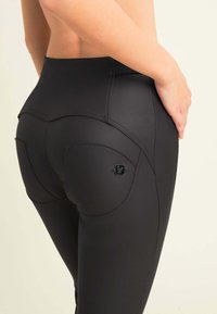 Leggings negros de talle alto con una textura suave y elástica. Presenta bolsillos traseros redondeados y un detalle de costura sutil. Acento del logo metálico.