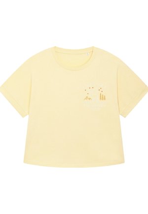 T-shirt jaune surdimensionné à manches courtes en coton doux. Il présente un motif imprimé avec des montagnes et des arbres, ainsi que le texte "EXPLOREZ L'INVISIBLE."