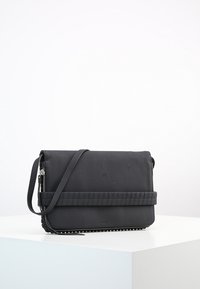 Borsa a tracolla nera con una finitura testurizzata e una chiusura con zip, caratterizzata da una tracolla piatta e un accento trapuntato sulla parte anteriore, di dimensioni compatte.