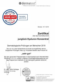 Zertifikat von Dermatest, mit einem blau-rot Siegel, Text in deutscher Sprache und einer Unterschrift am unteren Ende. Weißer Hintergrund.