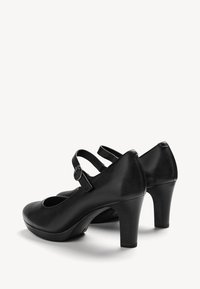 Paire de chaussures Mary Jane noires à talons hauts, bouts ronds et brides ajustables à boucle, sur fond blanc.