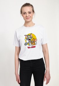 Hvid bomulds t-shirt med et farverigt grafik af tegnefilmsfigurerne Tom og Jerry mod en gul cirkel, med rød tekst nedenunder.
