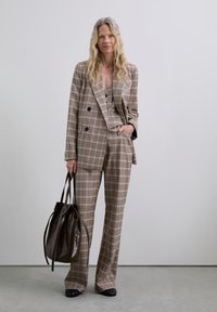 Brown plaid tailored suit with a double-breasted blazer and wide-leg trousers, paired with a brown leather bag and black shoes.
