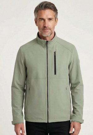 Man die een lichtgroen jack met ritssluiting draagt, met ritssluitingen op de borstzakken en zijzakken, staand tegen een effen lichte achtergrond.