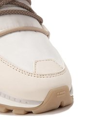 Zapatilla deportiva beige con un upper sintético suave, que cuenta con una puntera prominente y cordones texturizados y trenzados. Suela de goma con surcos de tracción.