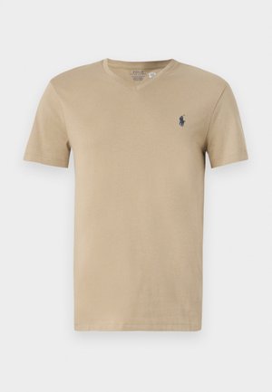 Camiseta de algodón beige con mangas cortas y cuello en V, que presenta un pequeño logo azul marino en el lado izquierdo del pecho. Textura suave, corte estándar.