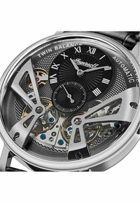 Automatisch horloge met een zwarte wijzerplaat met zilverkleurige Romeinse cijfers, een roestvrijstalen kast en een transparante achterkant die de details van het uurwerk toont.