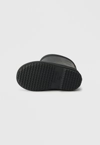 Sola de bota de borracha preta com um padrão texturizado para maior aderência. Apresenta uma forma arredondada e um acabamento suave, com o logótipo da marca em relevo.