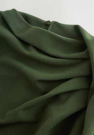 Dark green fabric with soft folds and a small green button sewn near the edge on a light background.